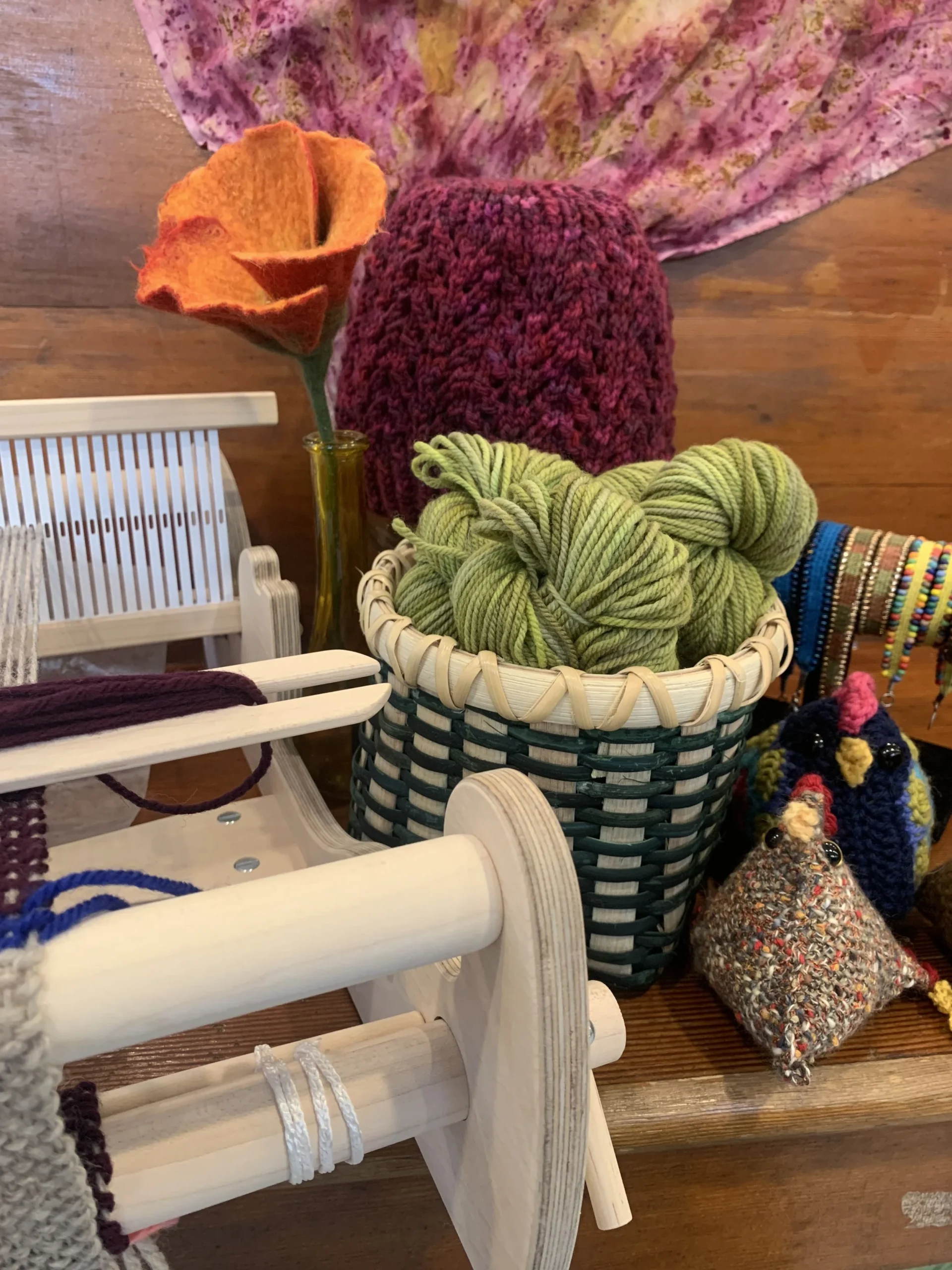 Felted flowers, hand-dyed yarn and a small weaving loom on a wooden table at Clear Creek Farm